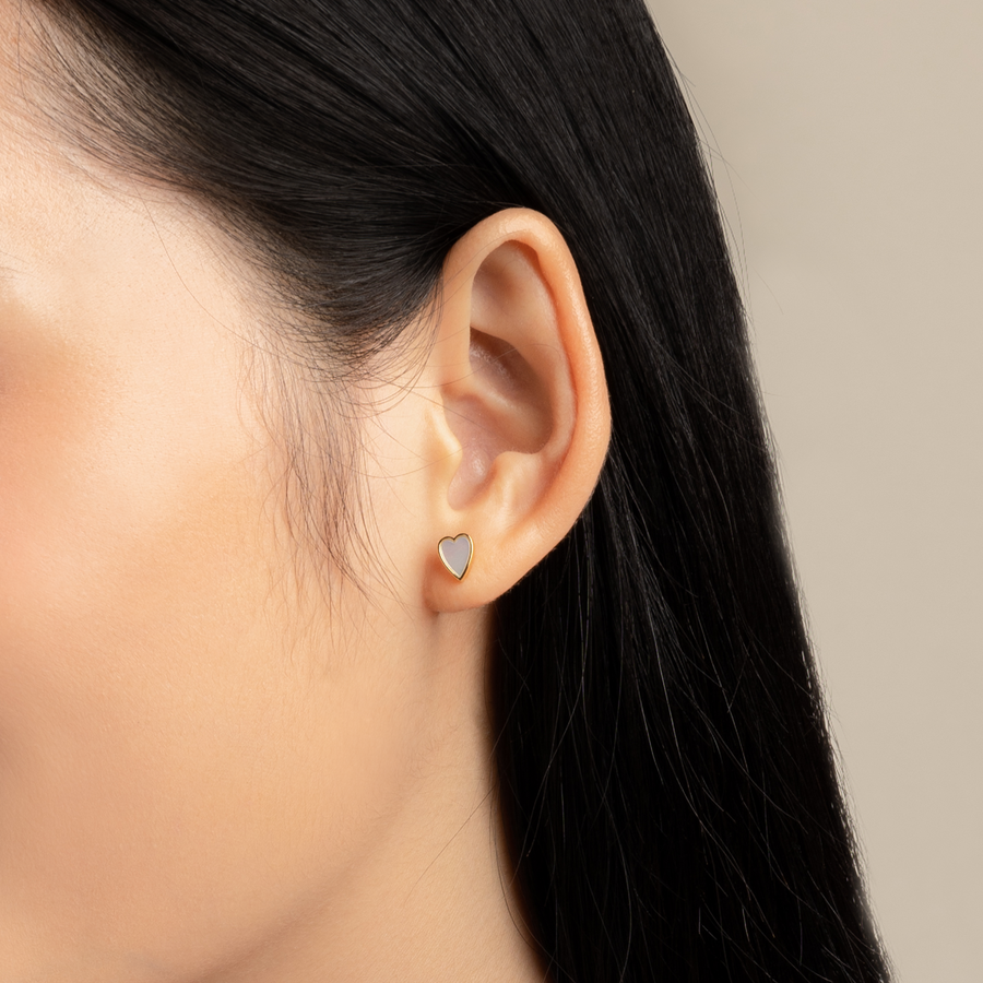 Charming and dainty earrings. Model wears gold, heart-shaped studs with mother of pearls.